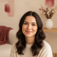 A happy woman in her late 20s to early 30s smiles warmly, looking content and trustworthy.